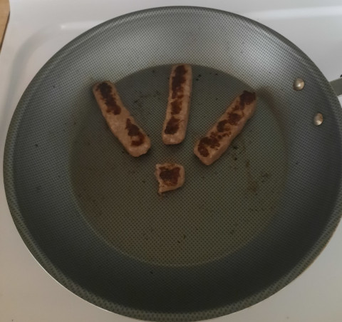 an image of sausage cooking while arranged in the shape of the sitelen pona glyph for 'seli.'